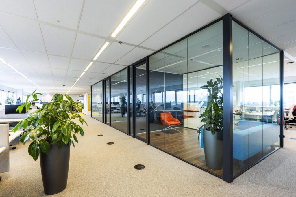 Modern kantoorinterieur aan de Johan Huizingalaan met glazen vergaderruimtes, planten en een oranje loungestoel.
